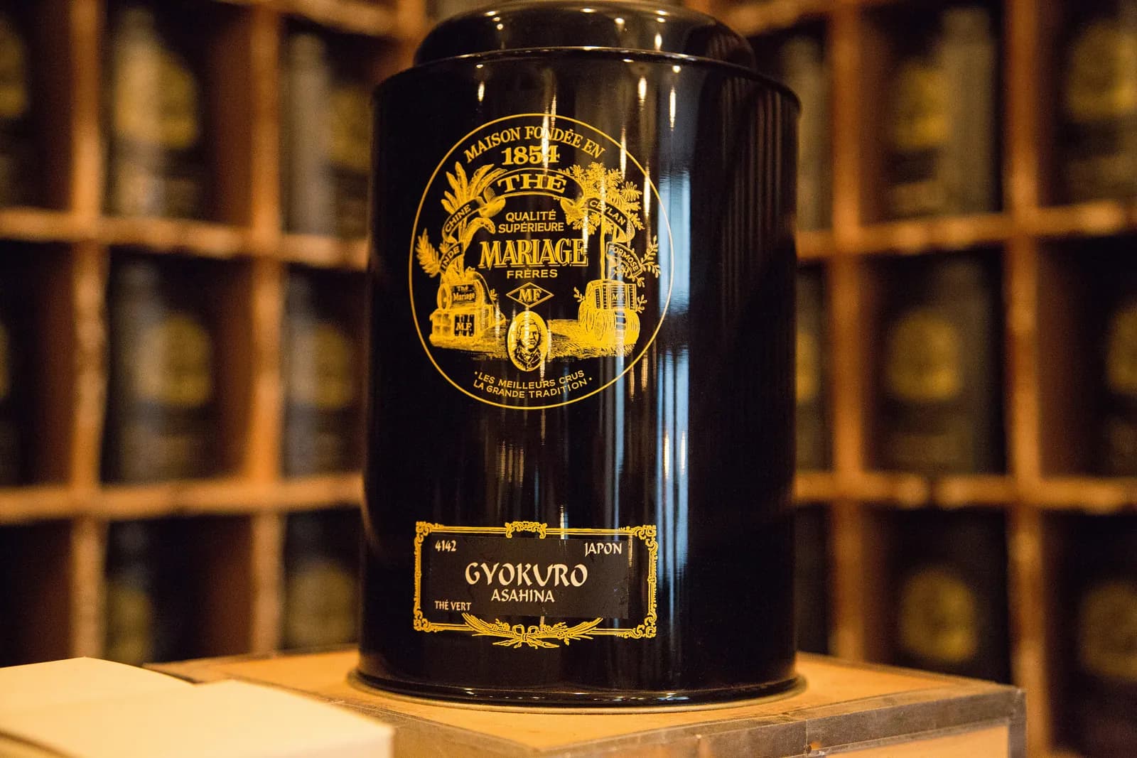 A black Mariage Frères tin labelled Gyokuro Asahina, with the gold 'Maison fondée en 1854' seal, in front of shelves of tins.