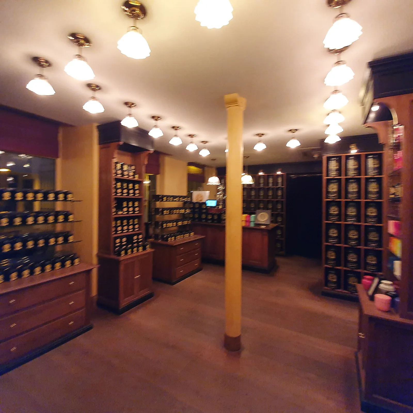 The shop floor of the Madeleine counter: wooden cabinets and shelves of tea tins under rows of glass pendant lamps.