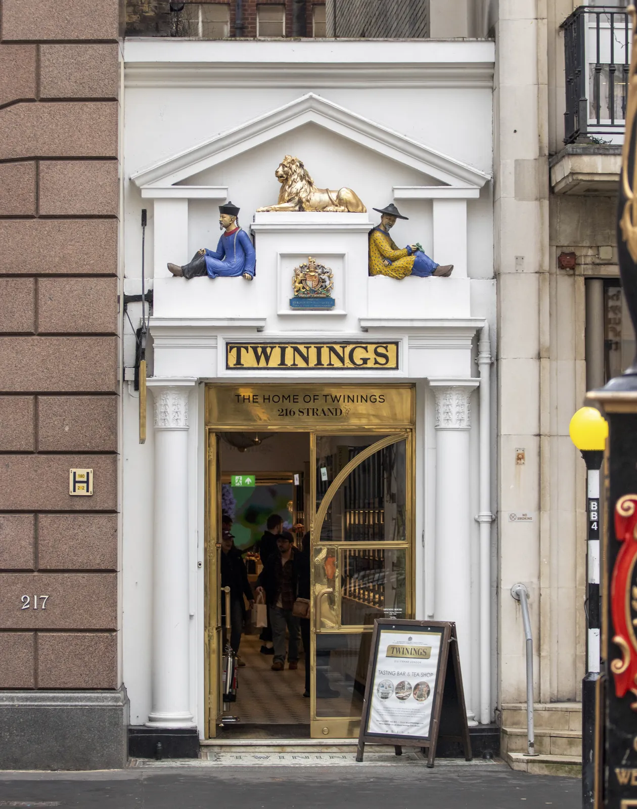 The full white stone doorway of Twinings at 216 Strand, with the gold sign 'The Home of Twinings, 216 Strand' over open glass doors.