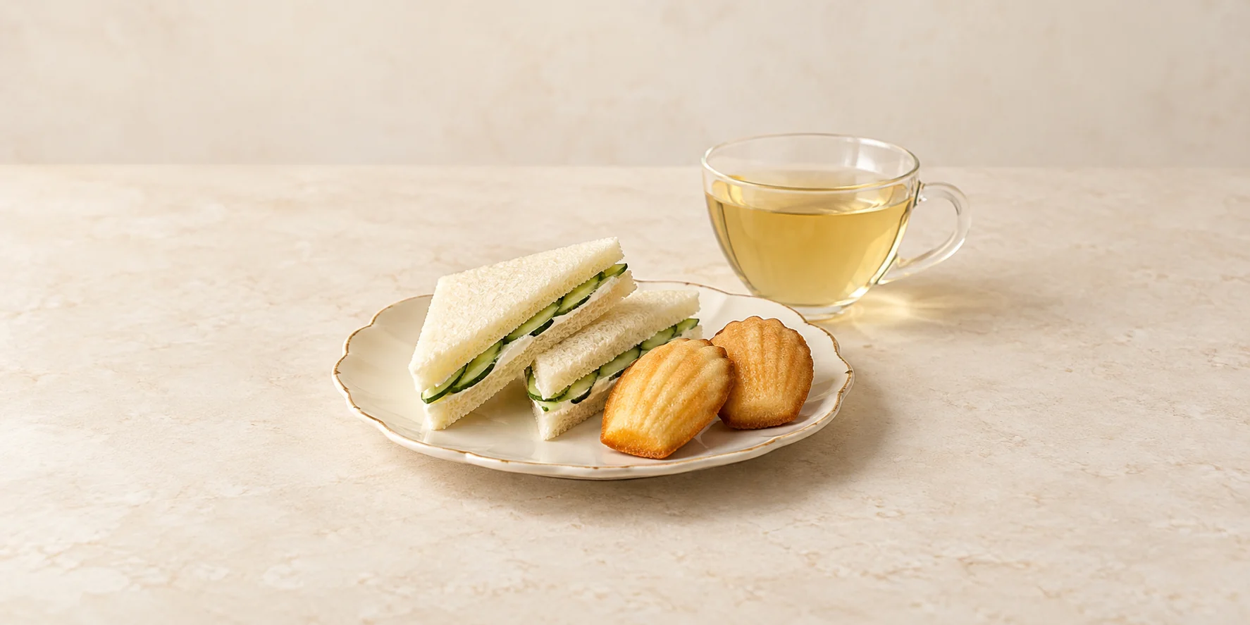 Cucumber finger sandwiches and plain madeleines beside pale golden Darjeeling white tea.