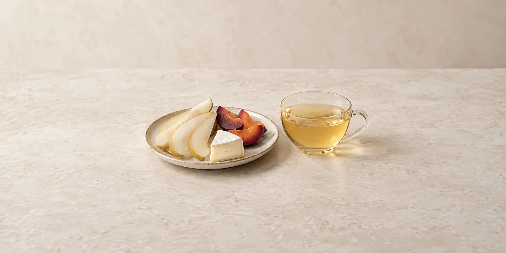 Pear and plum slices with mild brie beside pale golden Moonlight White tea.