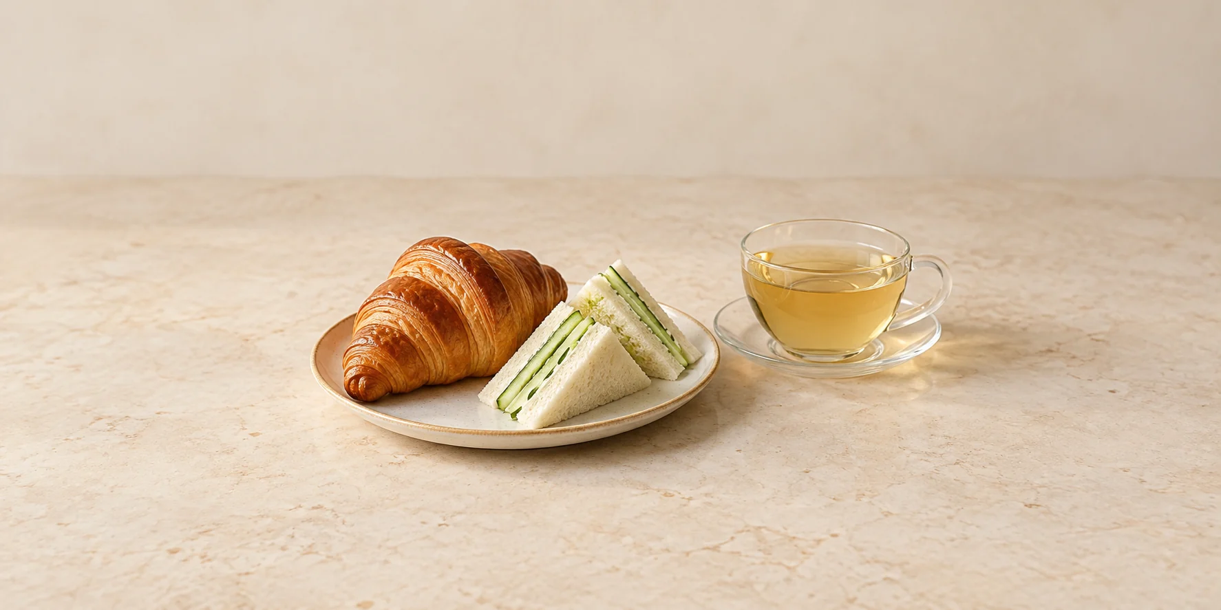 A plain croissant and cucumber finger sandwiches beside Pai Mu Tan white tea.