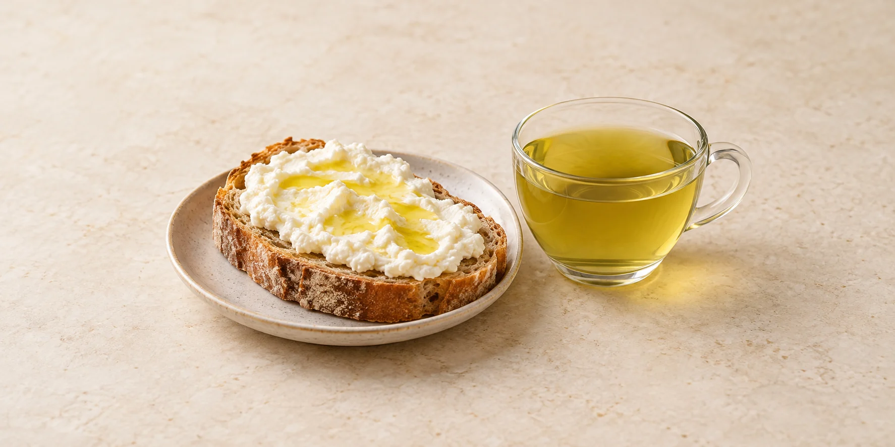 Rustic bread with ricotta and olive oil beside a glass cup of yellow-green nettle tea.