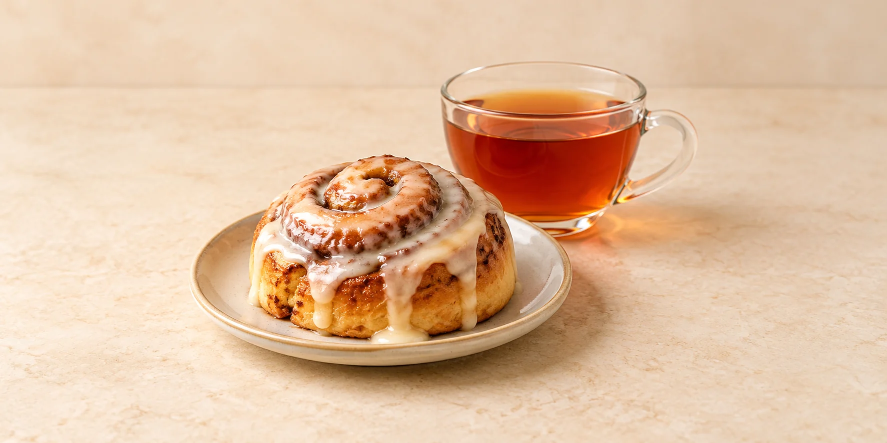 A glazed cinnamon roll beside a cup of amber-red vanilla rooibos tea.