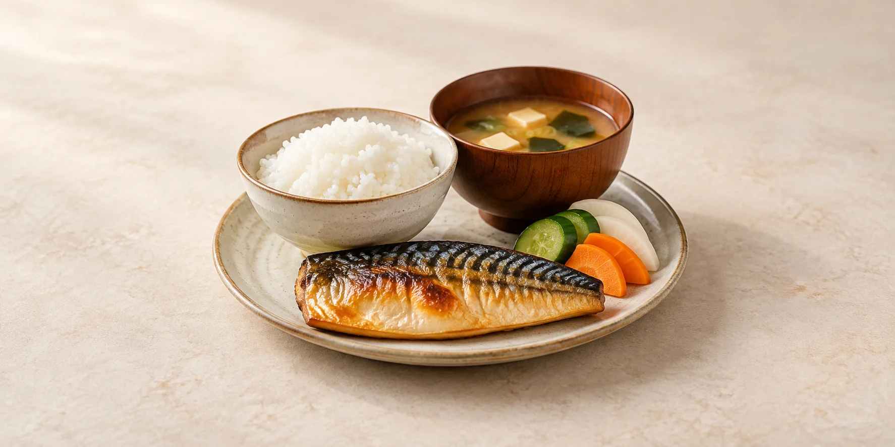Grilled fish, steamed rice, miso soup and pickled vegetables arranged as a Japanese meal.