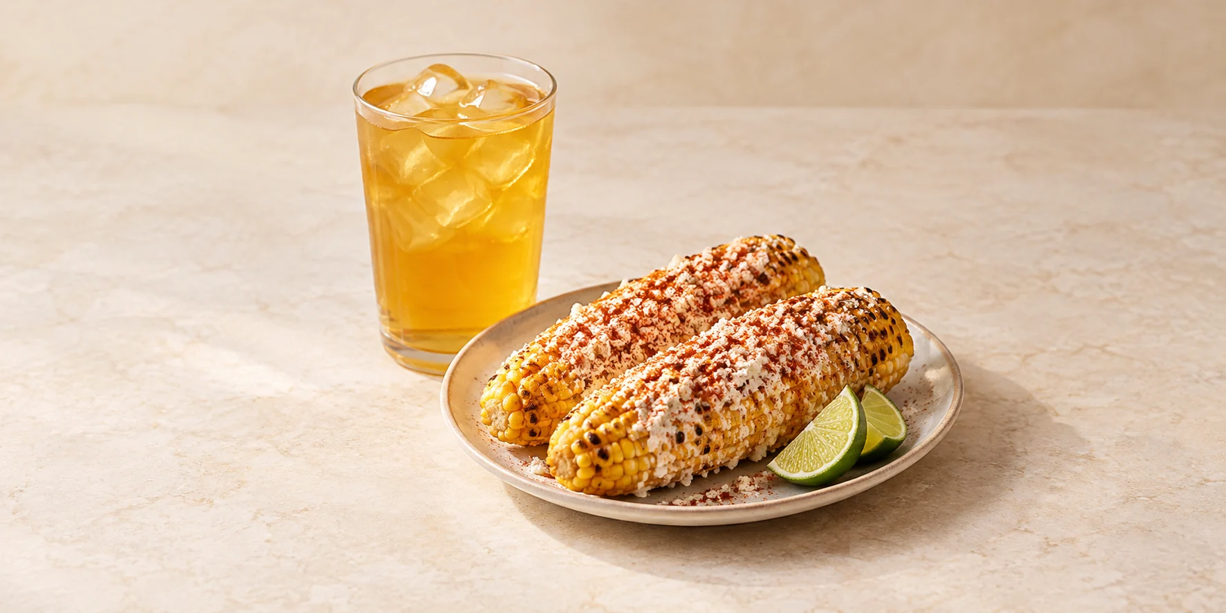 Mexican-style elote with chili, cheese and lime beside iced mango green tea.