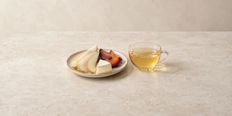 Pear and plum slices with mild brie beside pale golden Moonlight White tea.